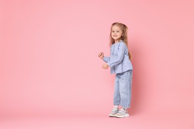 Photo of Cute little girl dancing on pink background, space for text