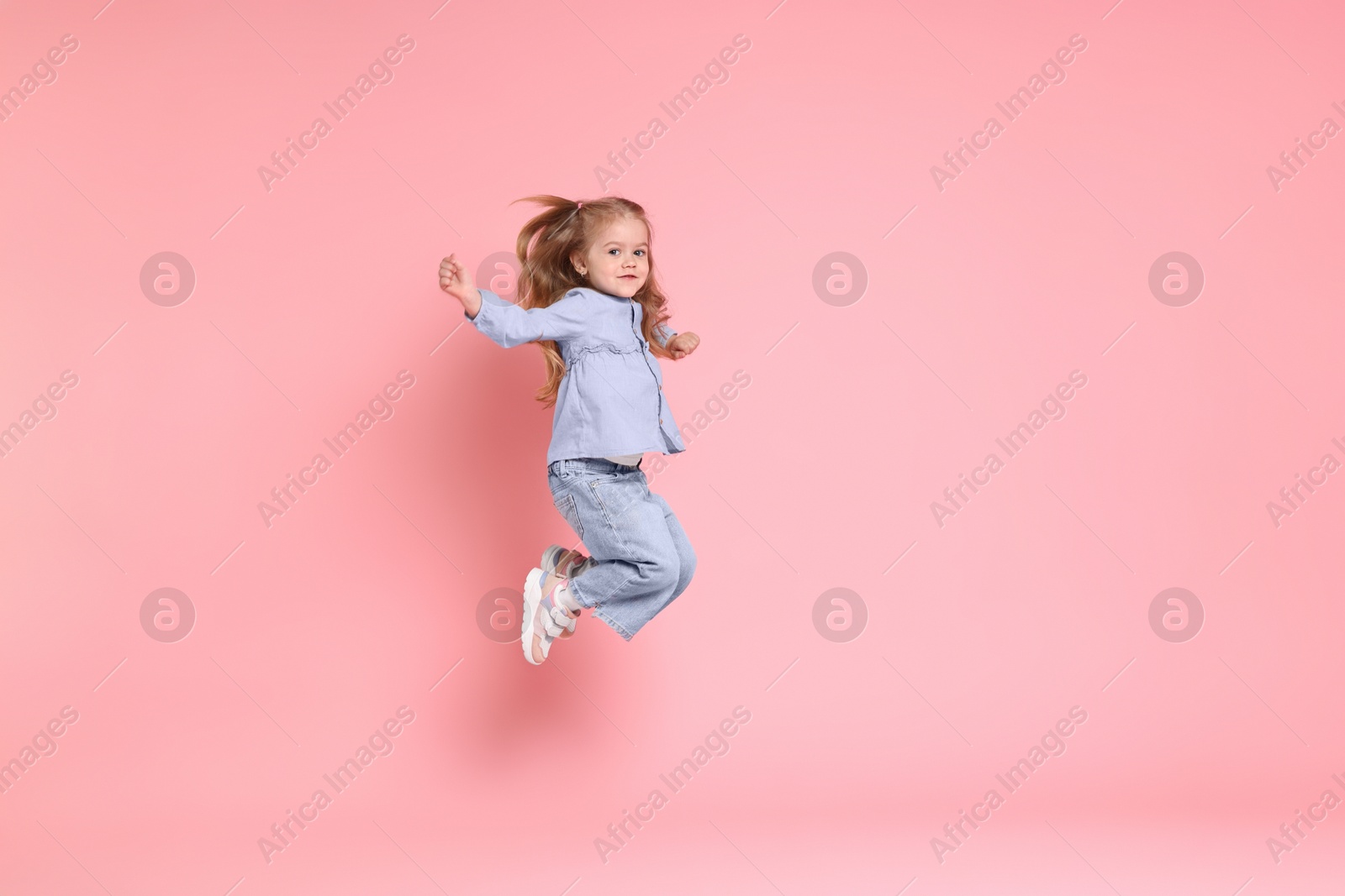 Photo of Cute little girl dancing on pink background, space for text