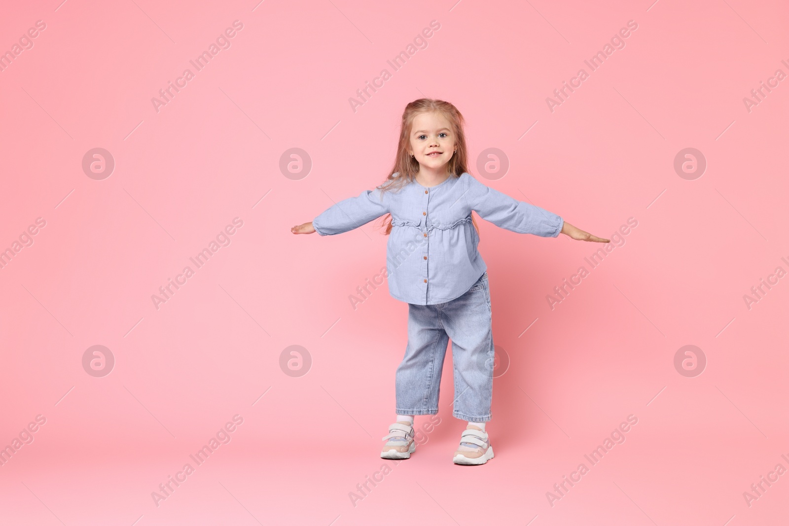 Photo of Cute little girl dancing on pink background