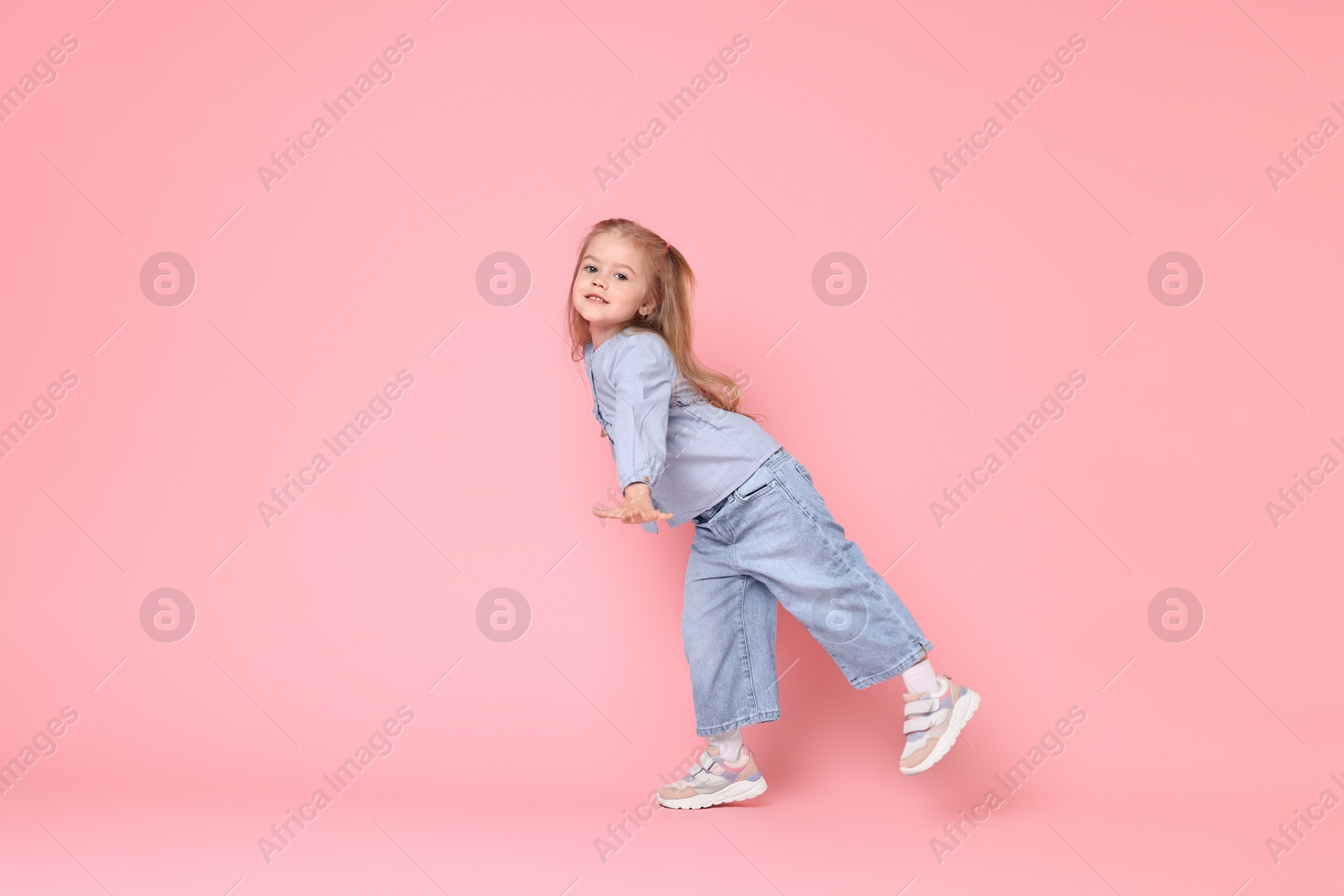 Photo of Cute little girl dancing on pink background, space for text