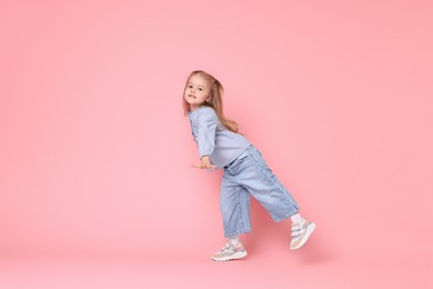 Cute little girl dancing on pink background, space for text