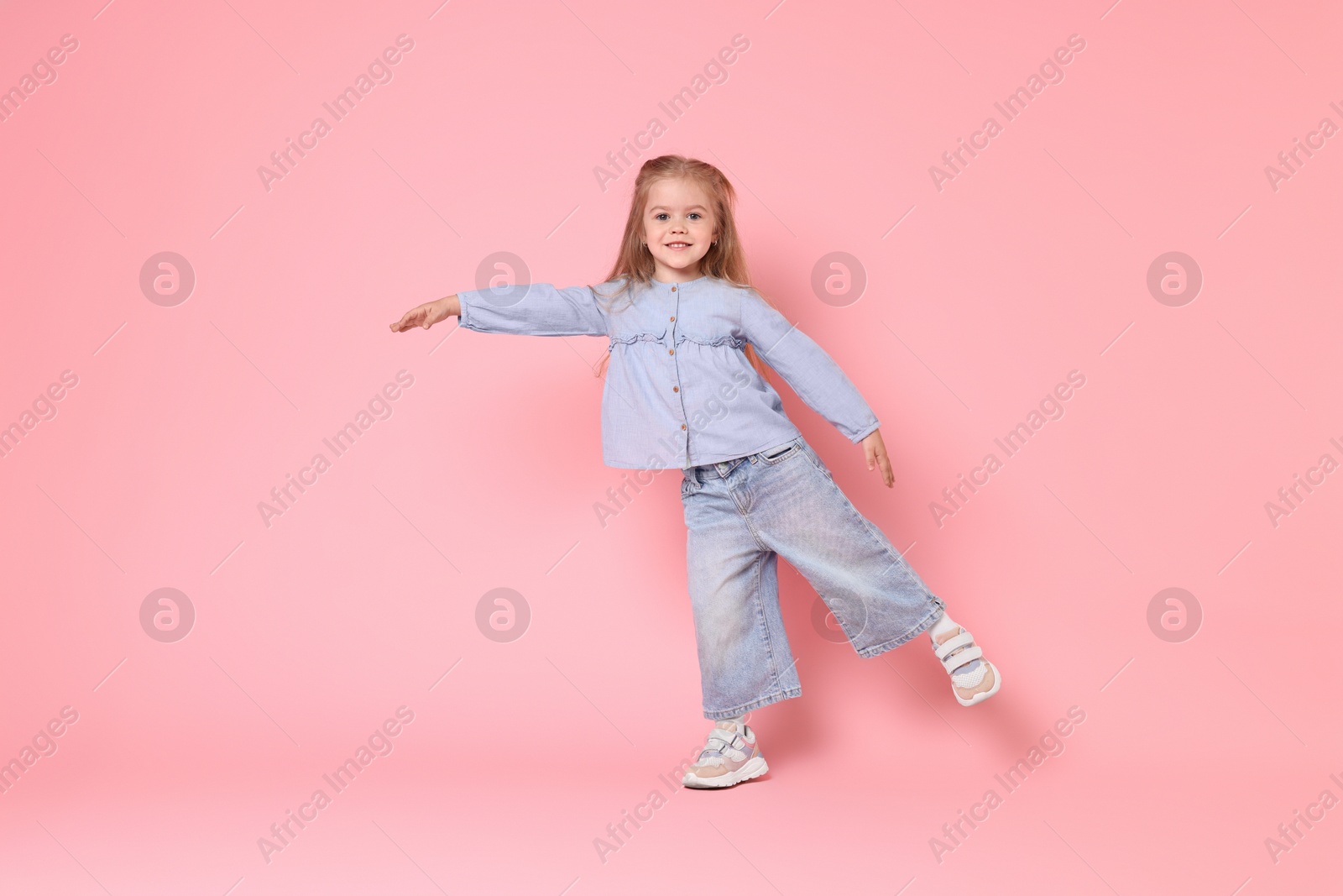 Photo of Cute little girl dancing on pink background