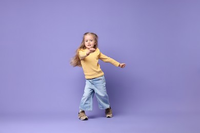 Photo of Cute little girl dancing on purple background