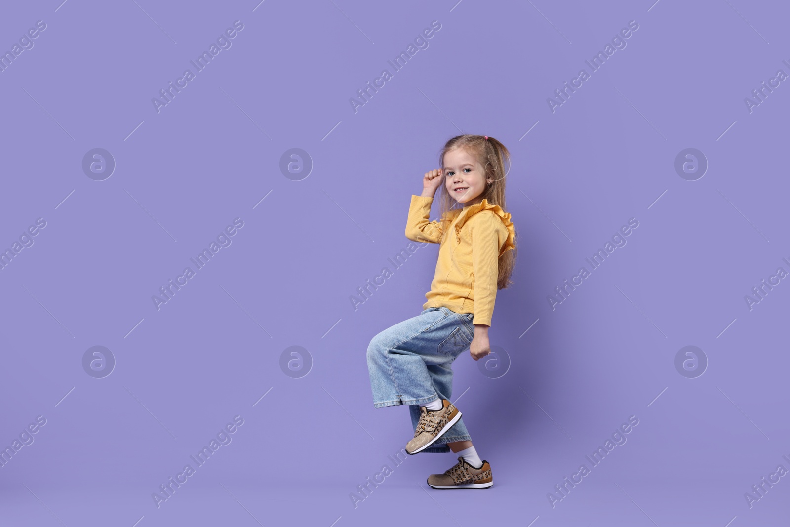 Photo of Cute little girl dancing on purple background, space for text