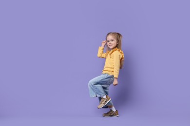 Photo of Cute little girl dancing on purple background, space for text