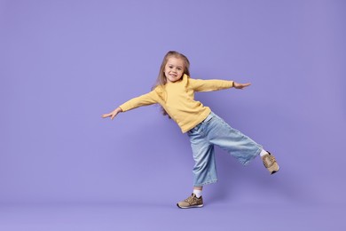 Photo of Cute little girl dancing on purple background, space for text