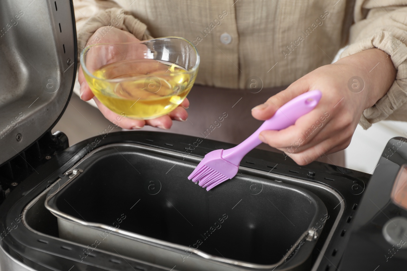 Photo of Woman spreading breadmaker pan with oil, closeup