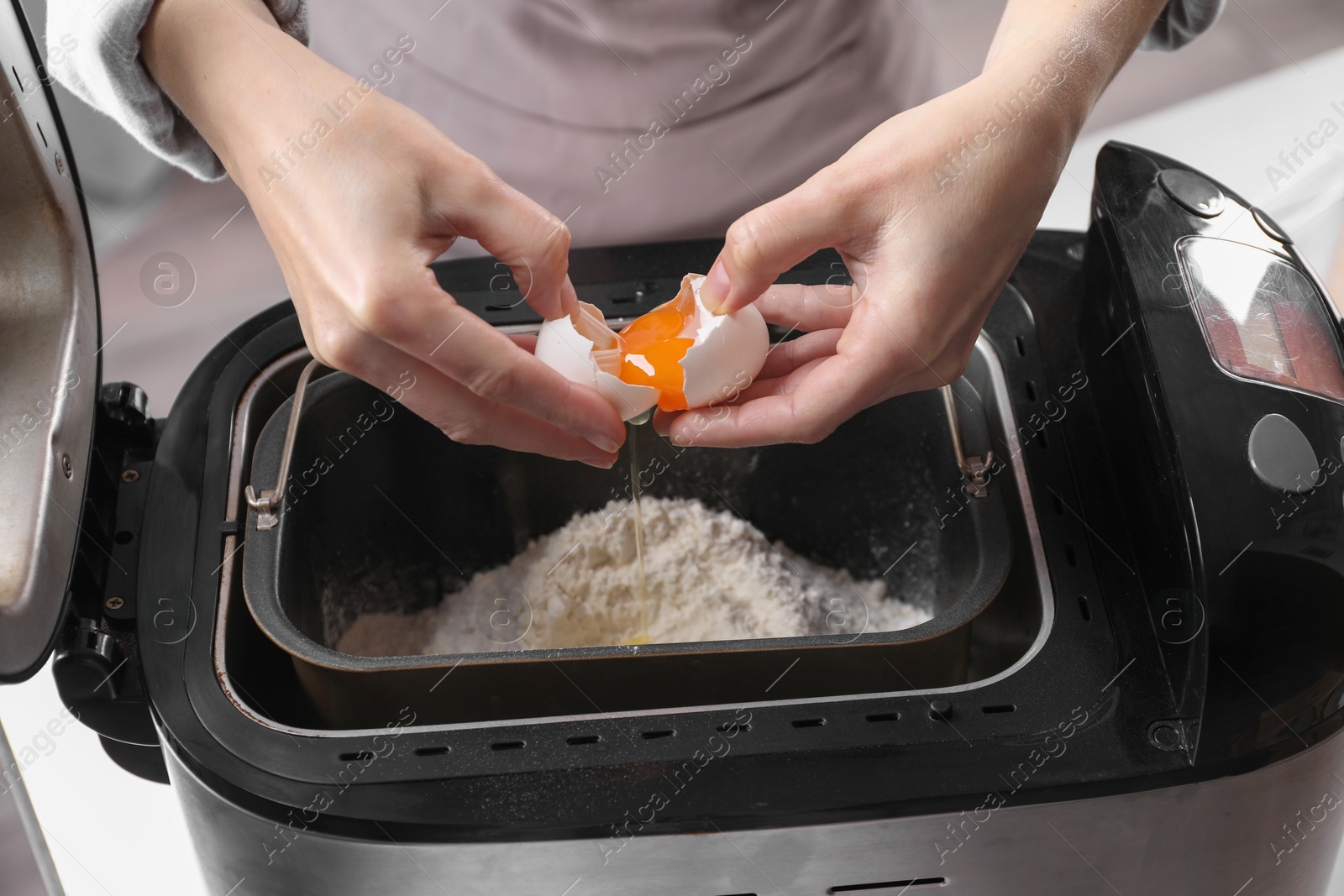 Photo of Woman adding egg into breadmaker indoors, closeup