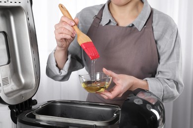 Woman with oil above breadmaker indoors, closeup