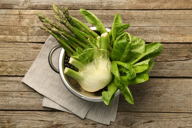 Photo of Metal colander with fennel, lettuce and asparagus on wooden table, top view