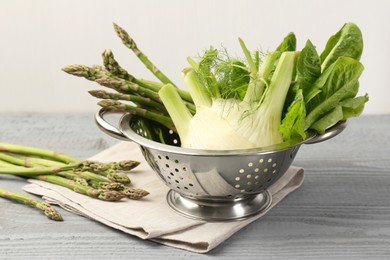 Photo of Metal colander with fennel, lettuce and asparagus on gray wooden table