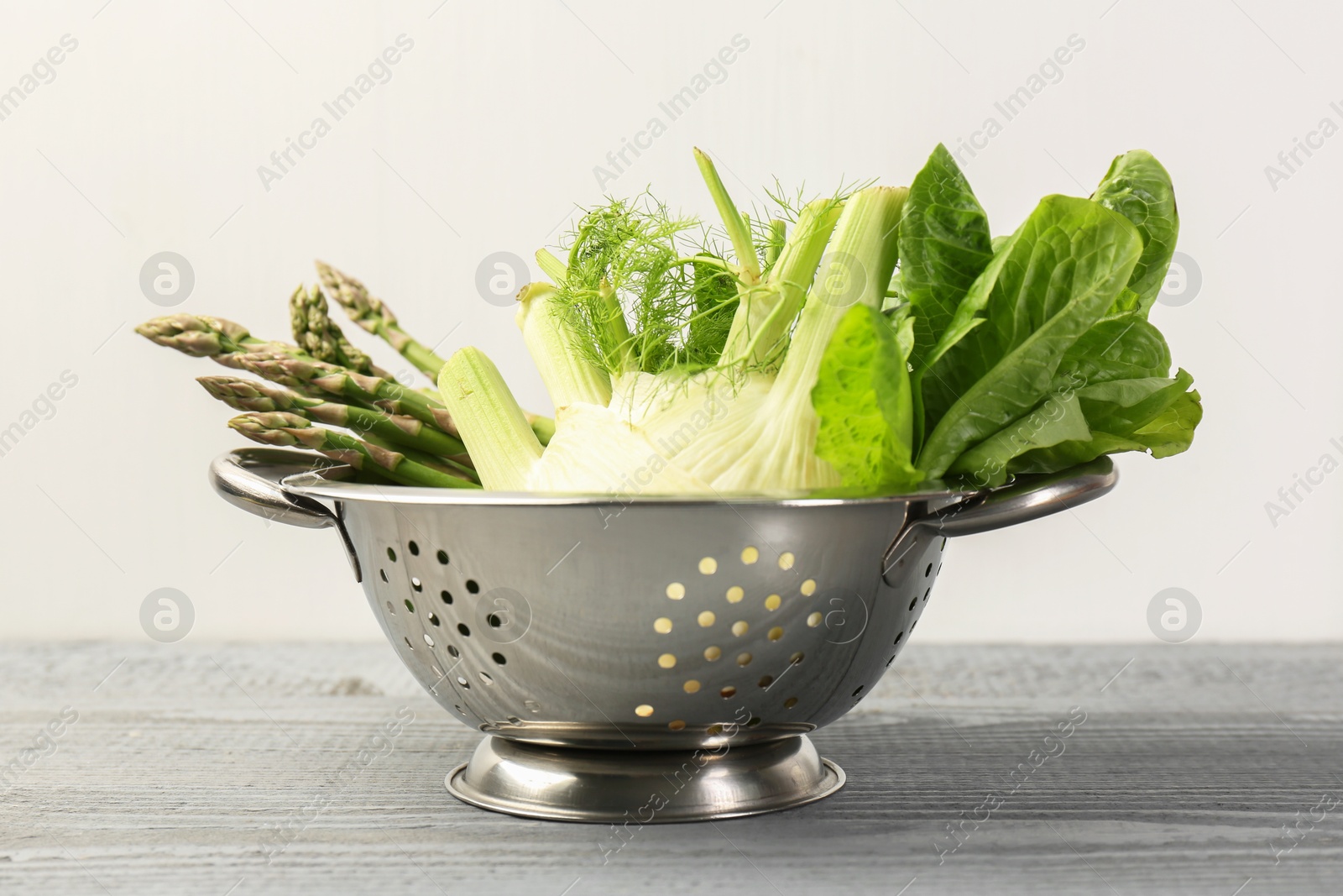 Photo of Metal colander with fennel, lettuce and asparagus on gray wooden table