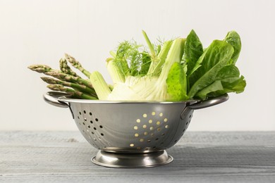 Photo of Metal colander with fennel, lettuce and asparagus on gray wooden table