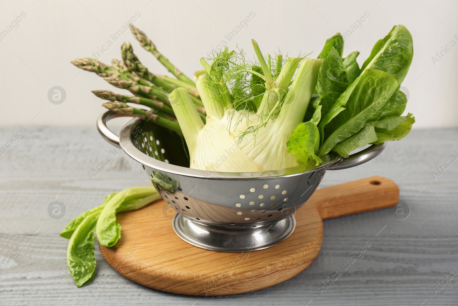 Photo of Metal colander with fennel, lettuce and asparagus on gray wooden table