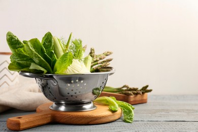 Photo of Metal colander with fennel, lettuce and asparagus on gray wooden table, space for text