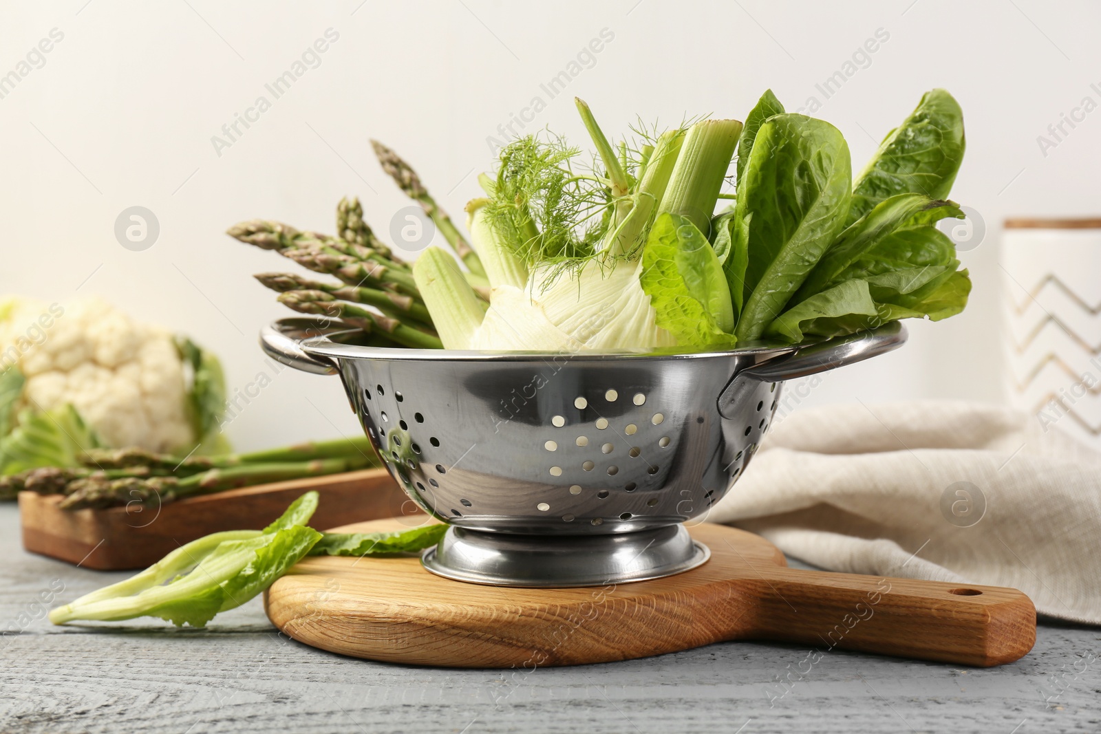 Photo of Metal colander with fennel, lettuce and asparagus on gray wooden table