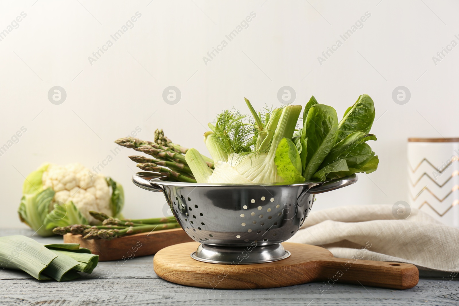 Photo of Metal colander with fennel, lettuce and asparagus on gray wooden table