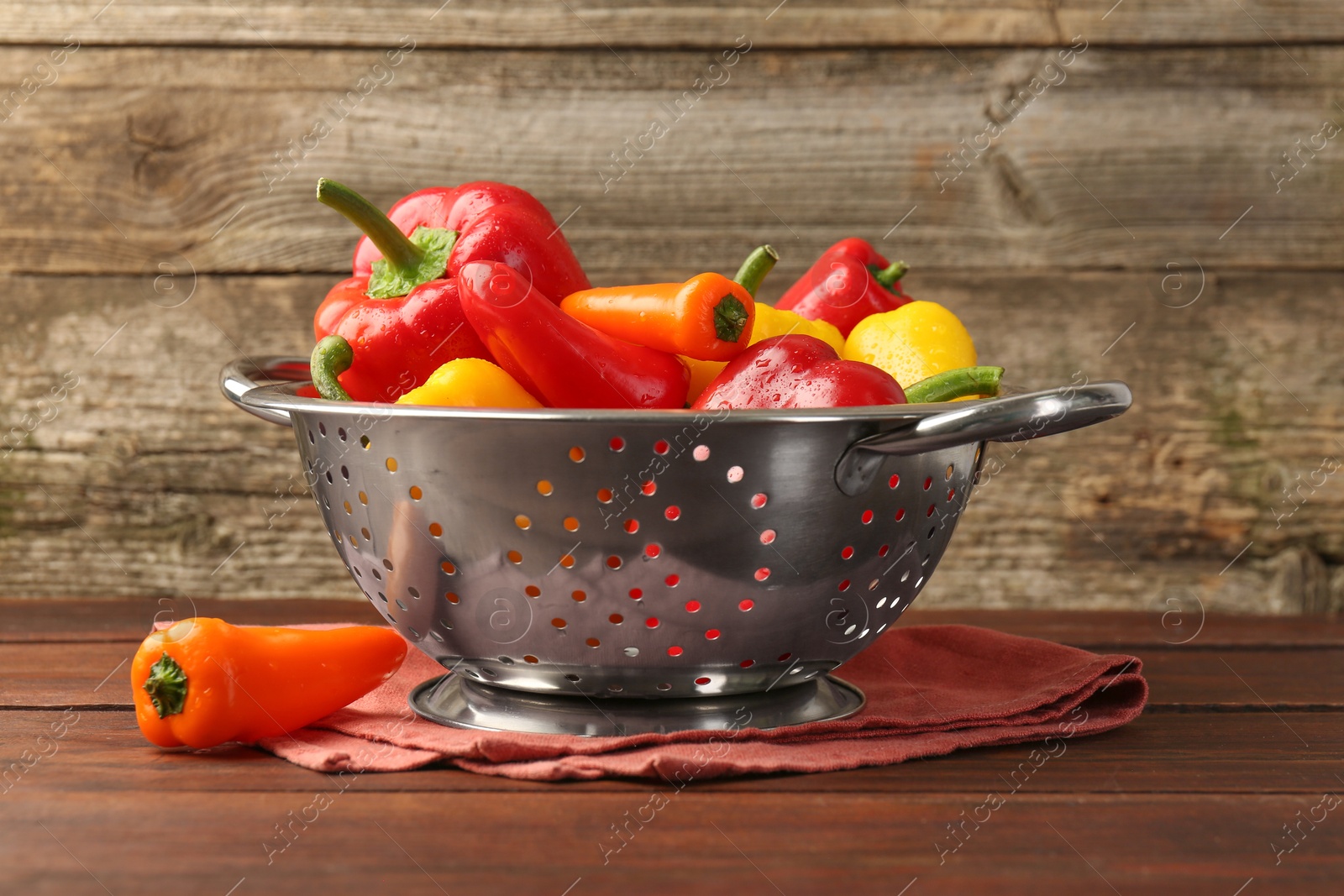 Photo of Metal colander with fresh peppers on wooden table