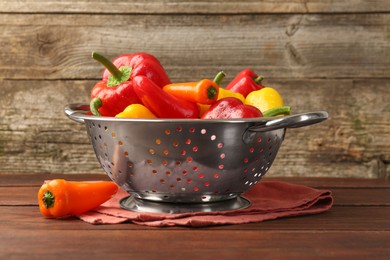 Photo of Metal colander with fresh peppers on wooden table