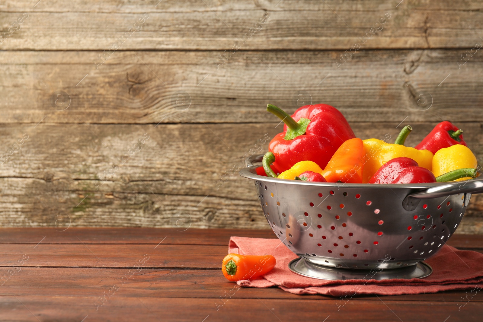 Photo of Metal colander with fresh peppers on wooden table, space for text
