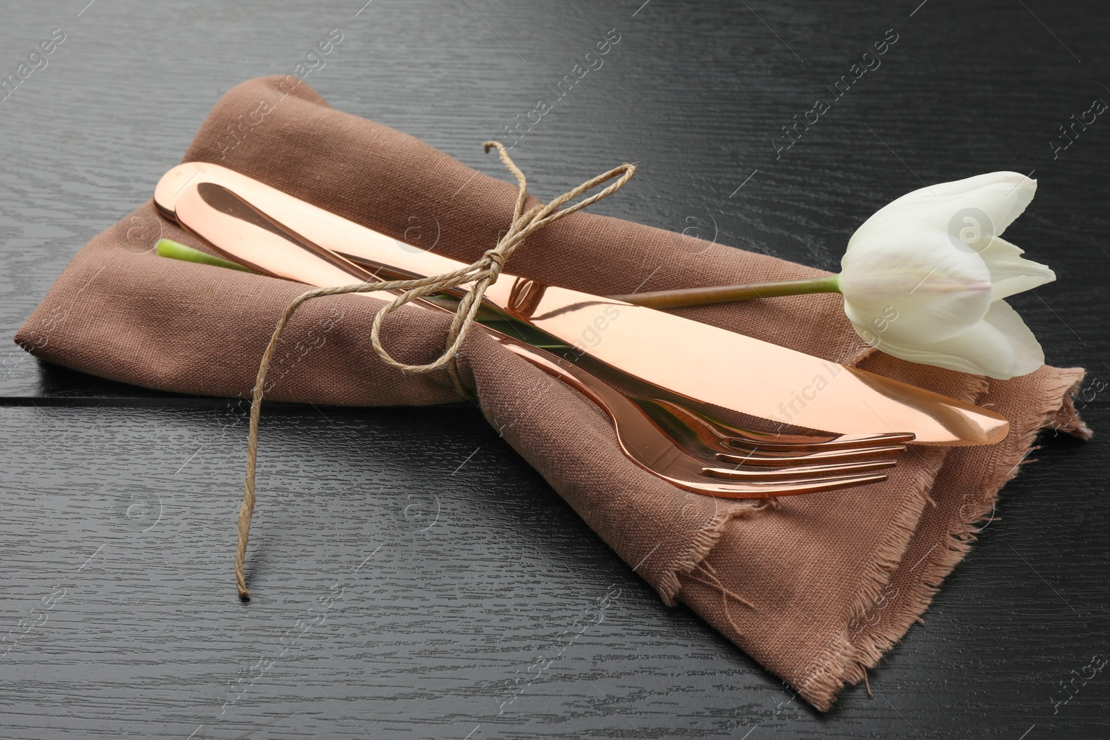Photo of Stylish setting with cutlery, flower and napkin on black wooden table