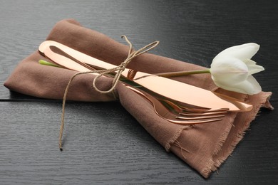 Photo of Stylish setting with cutlery, flower and napkin on black wooden table