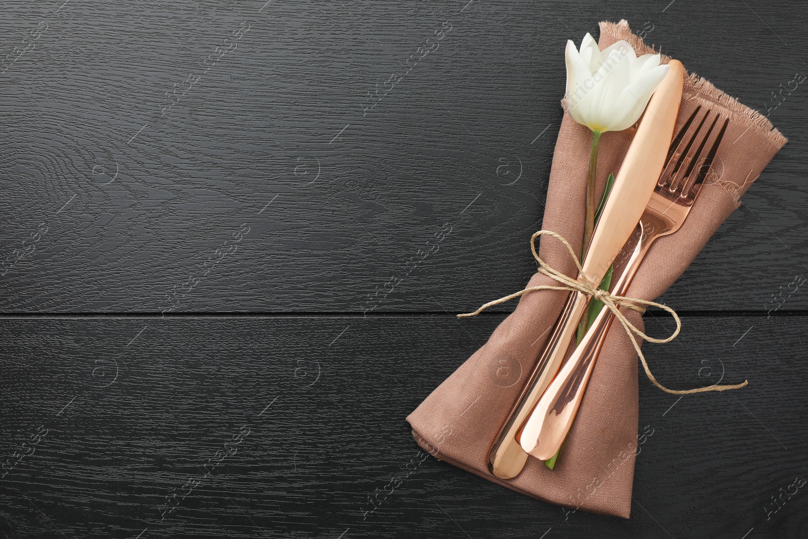 Photo of Stylish setting with cutlery, flower and napkin on black wooden table, top view. Space for text