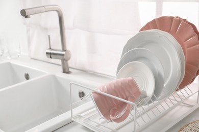 Photo of Drainer with different clean dishware and cup on light table near sink indoors