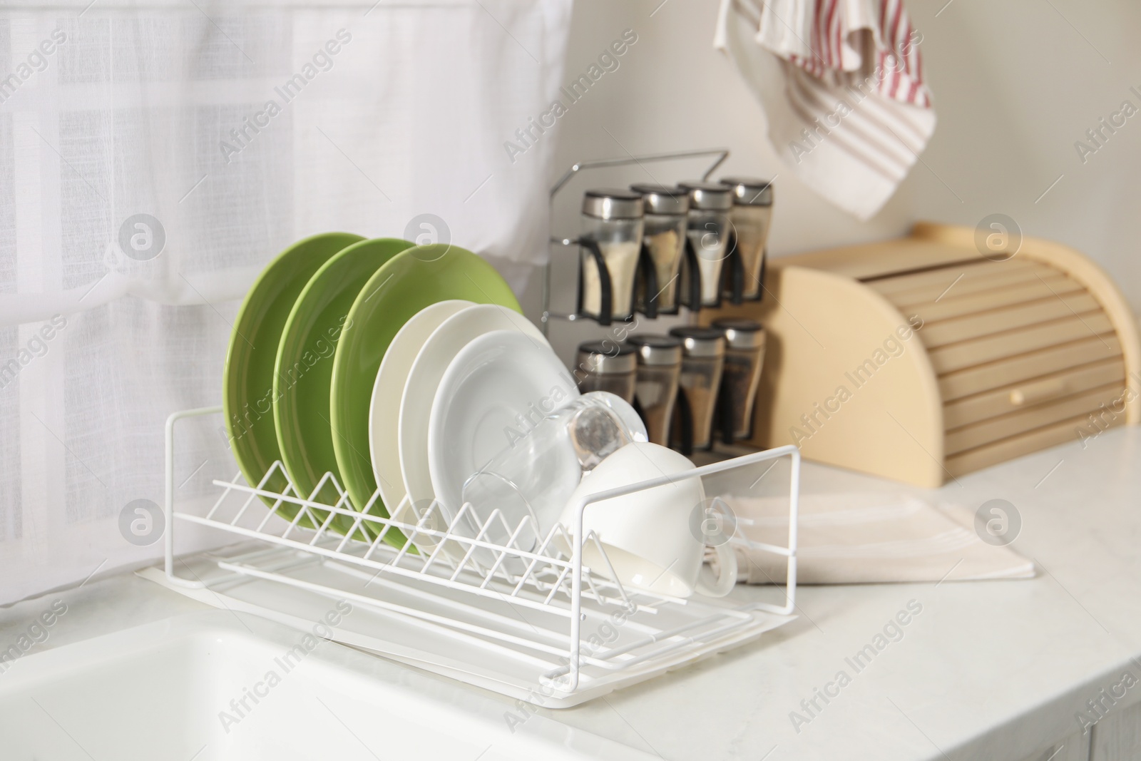 Photo of Drainer with different clean dishware, glass and cup on white table indoors