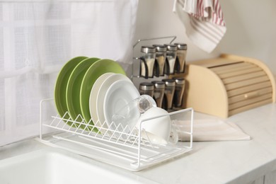 Drainer with different clean dishware, glass and cup on white table indoors