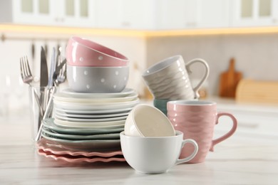 Many different clean dishware and cups on white marble table in kitchen