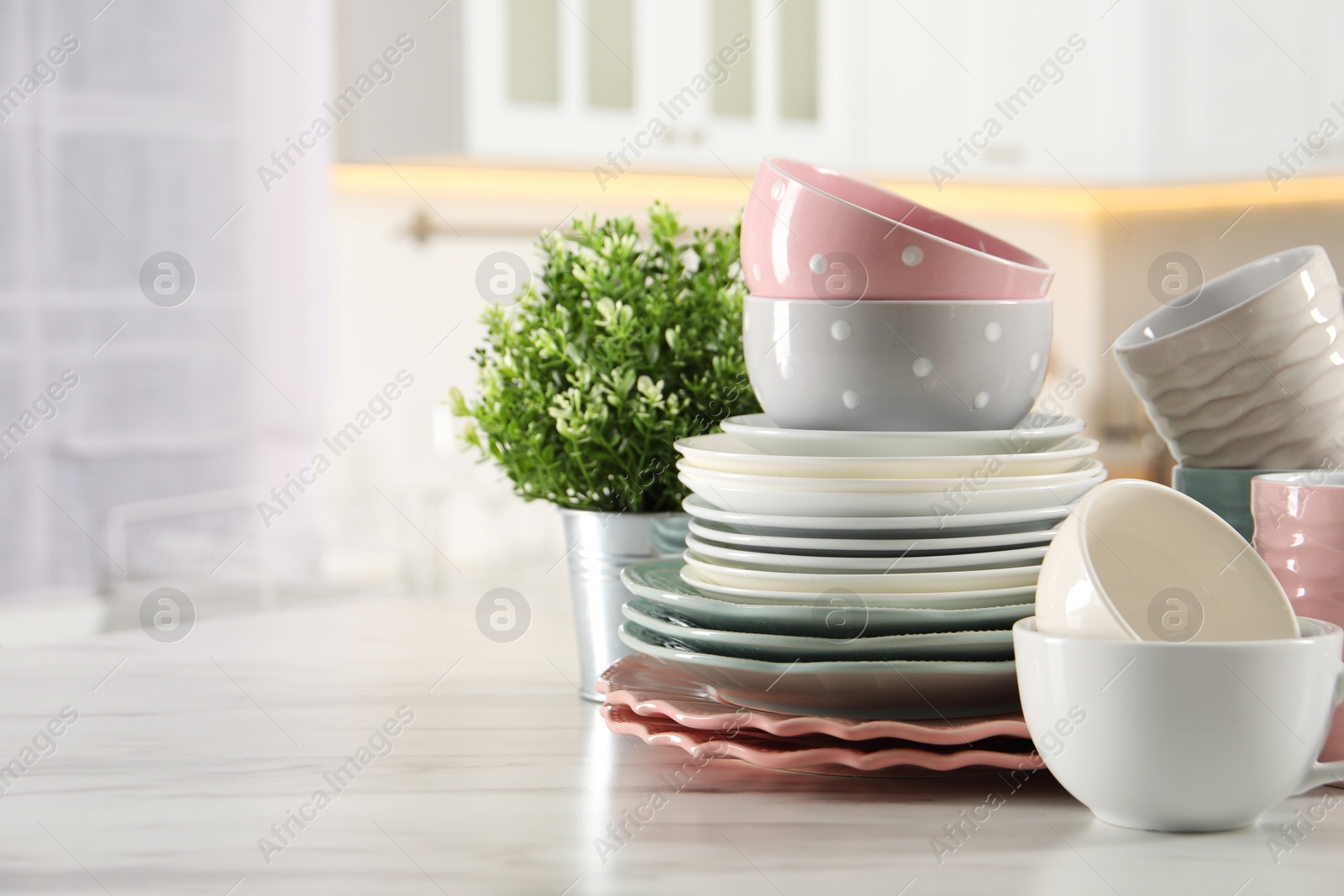 Photo of Many different clean dishware, cups and houseplant on white marble table in kitchen. Space for text