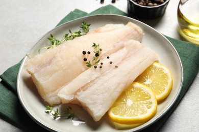 Photo of Plate with raw cod fish, spices, microgreens and lemon on grey table, closeup