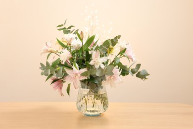 Photo of Bouquet of beautiful lily flowers in vase on wooden table against beige background