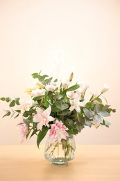 Photo of Bouquet of beautiful lily flowers in vase on wooden table against beige background