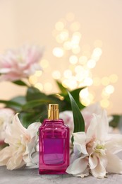 Photo of Bottle of perfume and beautiful lily flowers on table against beige background with blurred lights, closeup