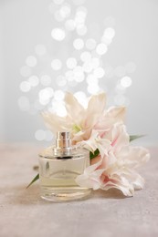 Photo of Bottle of perfume and beautiful lily flowers on table against beige background with blurred lights