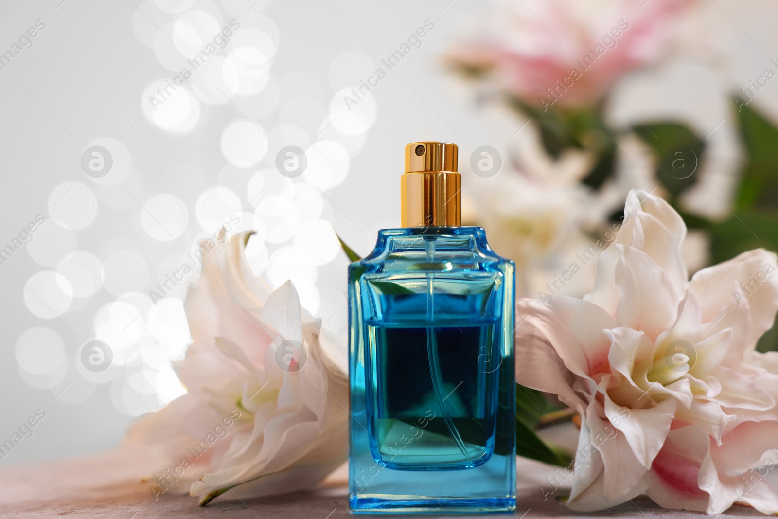 Photo of Bottle of perfume and beautiful lily flowers on table against beige background with blurred lights, closeup