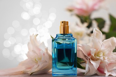 Photo of Bottle of perfume and beautiful lily flowers on table against beige background with blurred lights, closeup