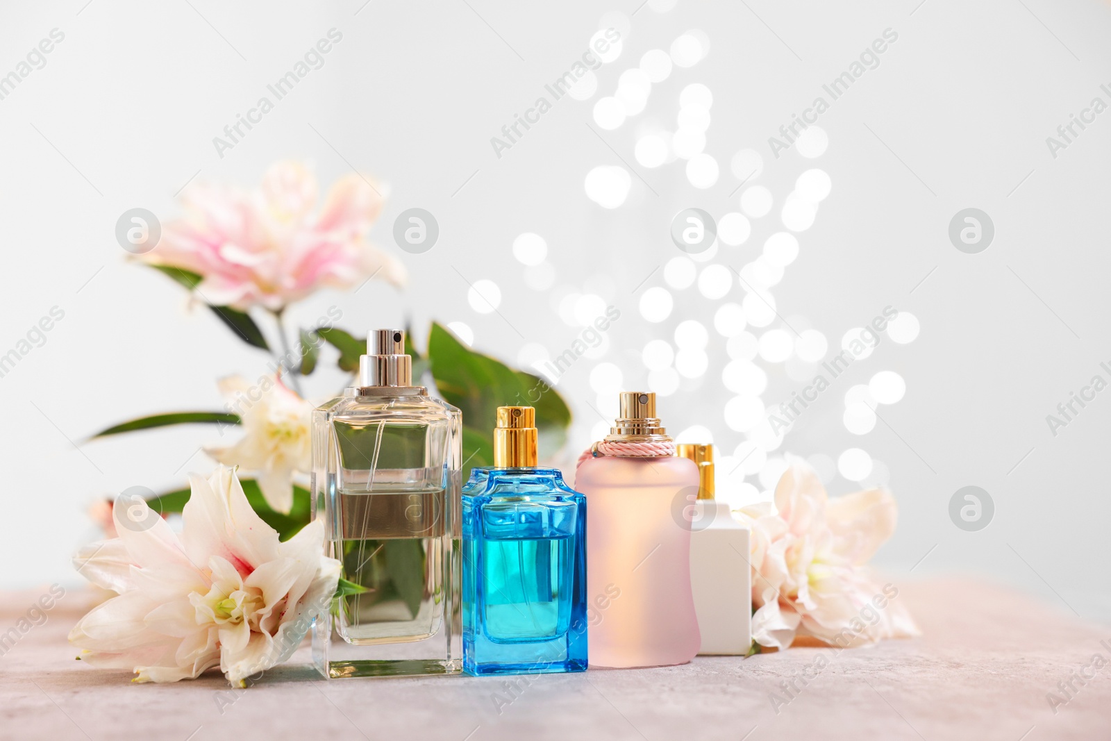 Photo of Perfume bottles and bouquet of beautiful lily flowers on table against beige background with blurred lights, closeup