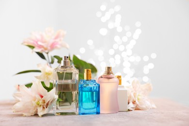 Photo of Perfume bottles and bouquet of beautiful lily flowers on table against beige background with blurred lights, closeup