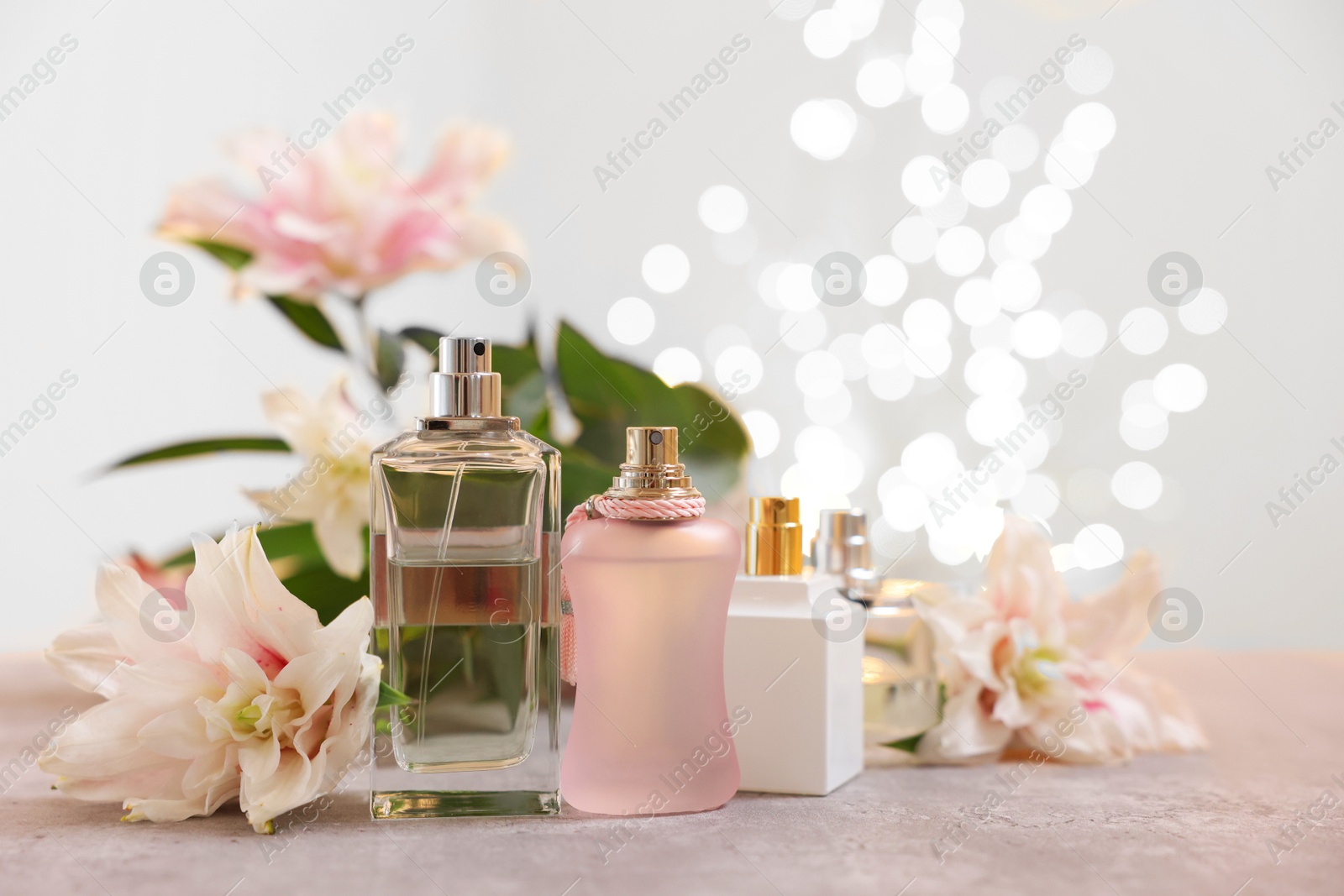 Photo of Perfume bottles and bouquet of beautiful lily flowers on table against beige background with blurred lights, closeup