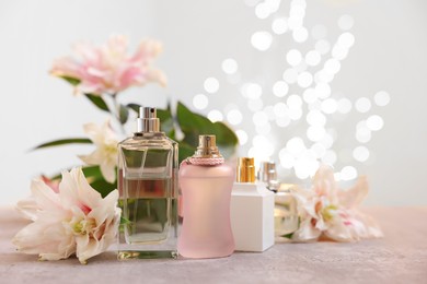 Photo of Perfume bottles and bouquet of beautiful lily flowers on table against beige background with blurred lights, closeup