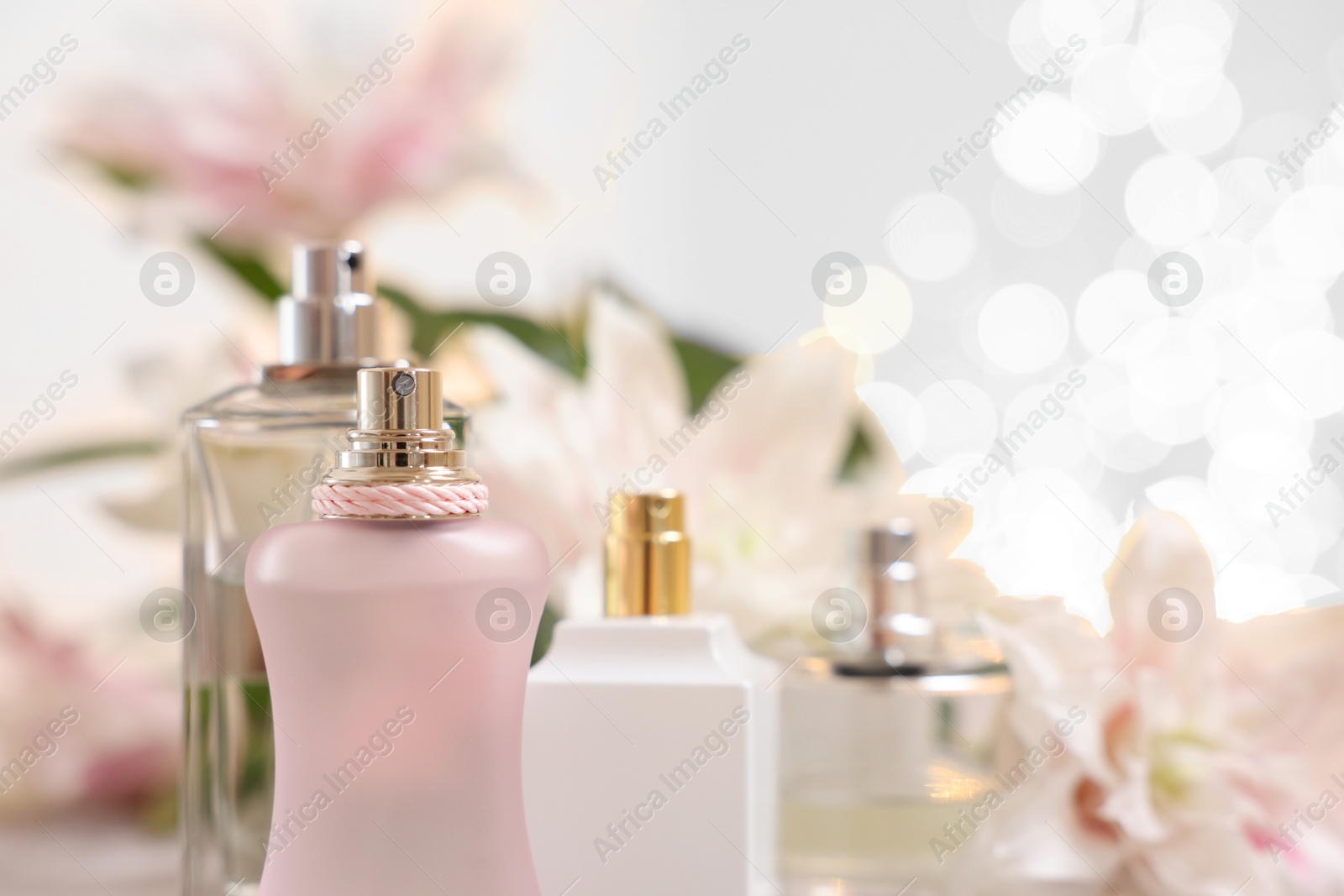 Photo of Bottles of perfume against beautiful lily flowers and blurred lights, closeup. Space for text