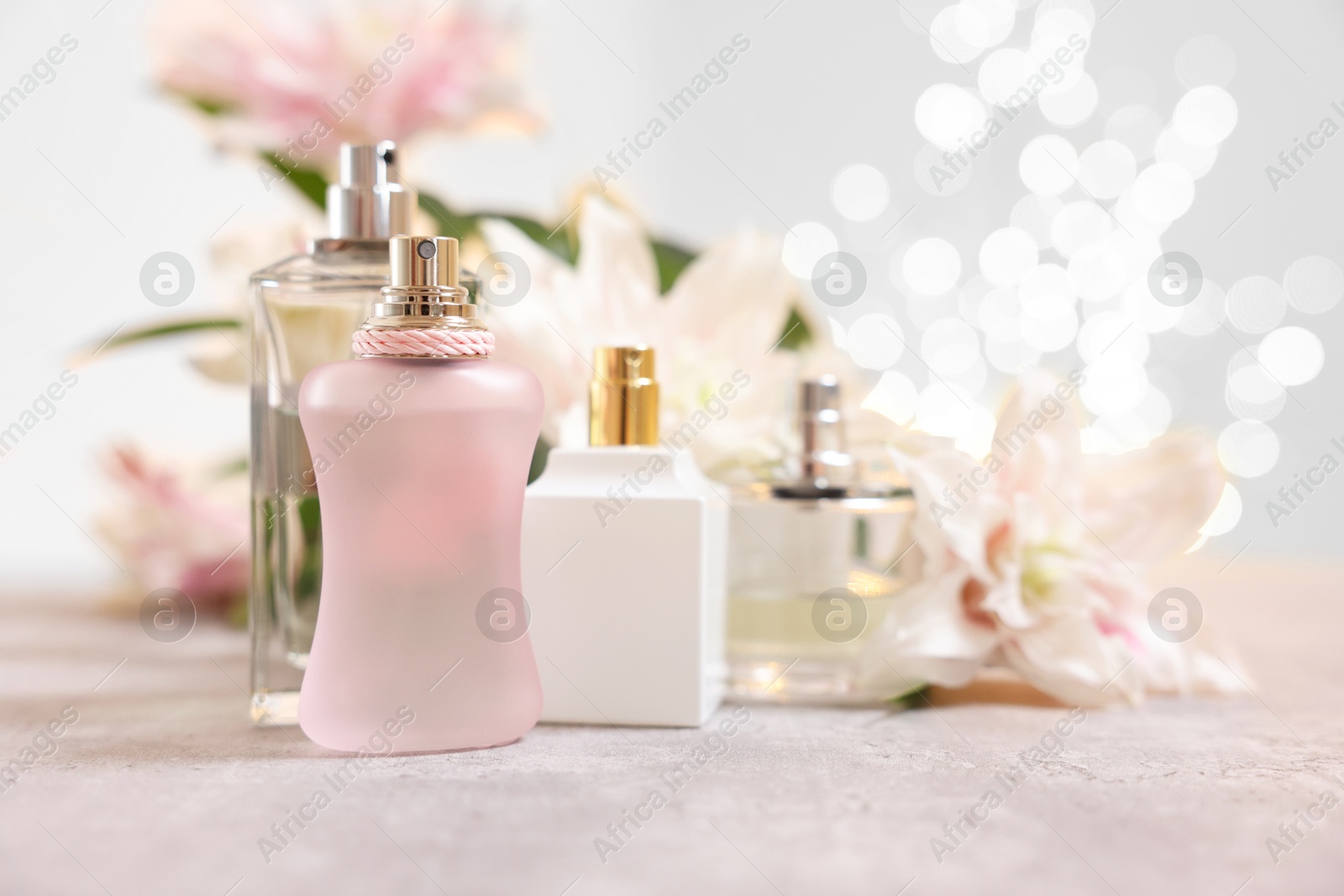 Photo of Perfume bottles and bouquet of beautiful lily flowers on table against beige background with blurred lights, closeup