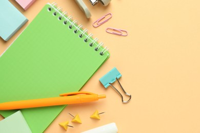 Photo of Flat lay composition with notebook, stapler and different stationery on pale orange background, space for text