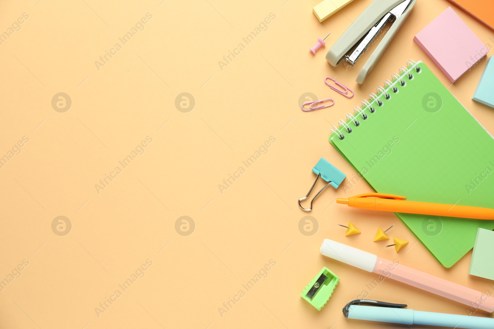 Photo of Flat lay composition with notebook, stapler and different stationery on pale orange background, space for text