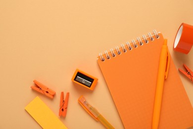 Photo of Flat lay composition with notebook and different stationery on pale orange background, space for text