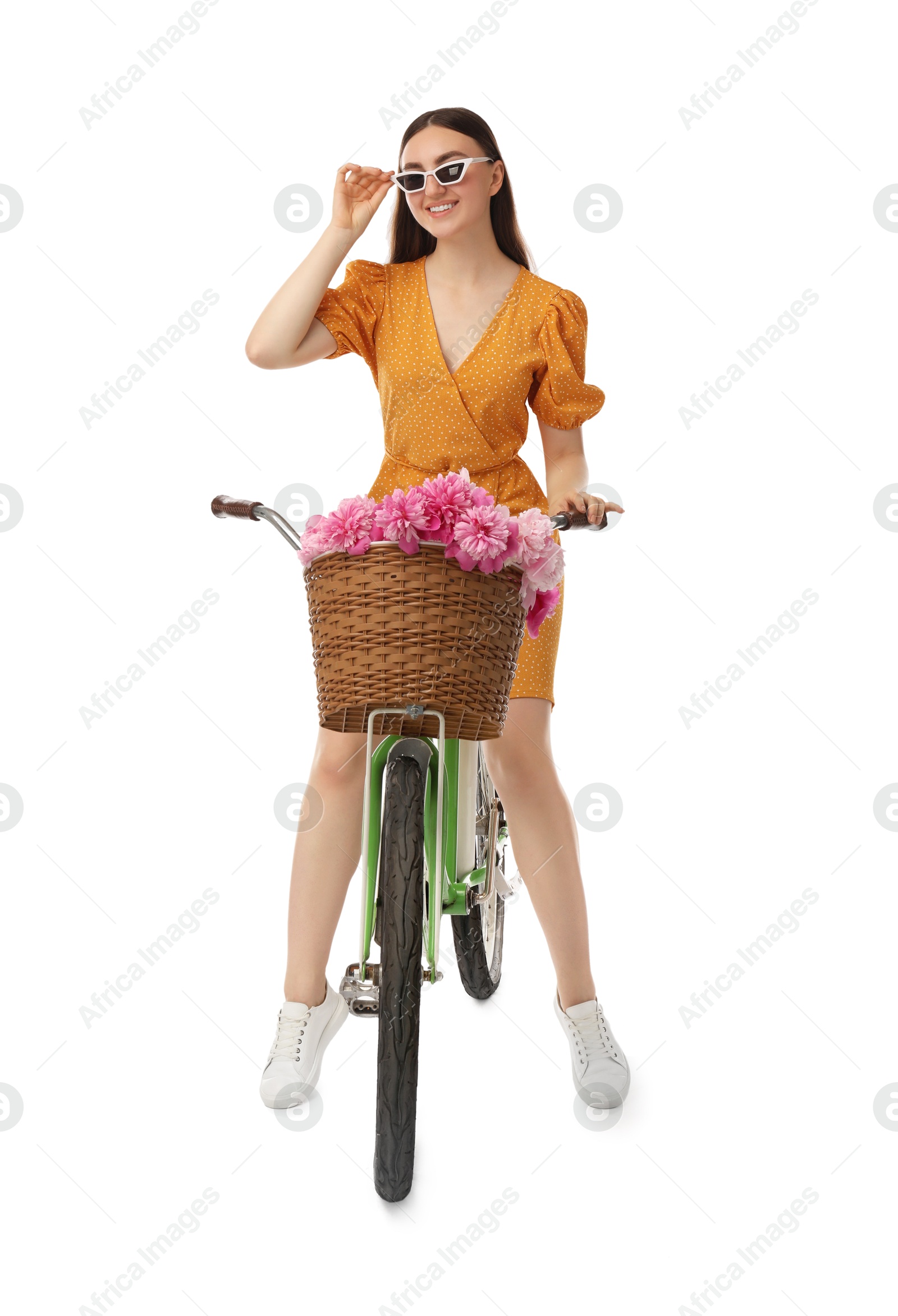 Photo of Smiling woman in sunglasses riding bicycle with basket of peony flowers on white background