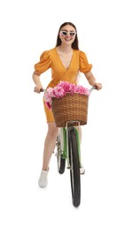 Smiling woman in sunglasses riding bicycle with basket of peony flowers on white background